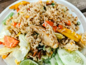 Close-up of Asian fried rice with chicken and fresh vegetables on a white plate.