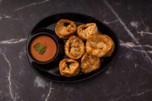 Delicious crispy cheese corn momos served with a spicy dipping sauce on a black plate.