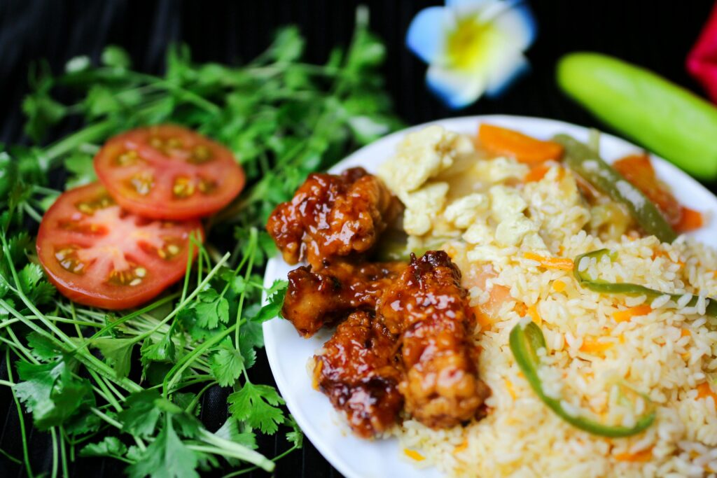 A vibrant Asian fusion dish with fried rice, glazed chicken, and fresh vegetables, garnished with cilantro.