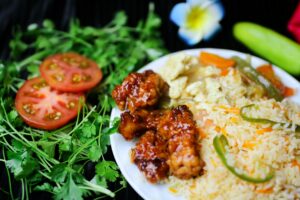 A vibrant Asian fusion dish with fried rice, glazed chicken, and fresh vegetables, garnished with cilantro.