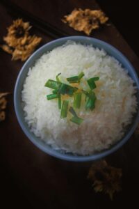 A close-up of a bowl of steamed white rice garnished with chopped green onions, showcasing elegant food presentation.