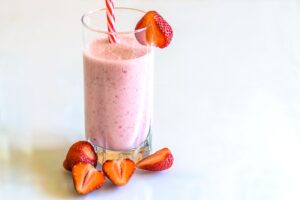 Delicious strawberry smoothie in a glass with fresh strawberries and a striped straw on a light background.