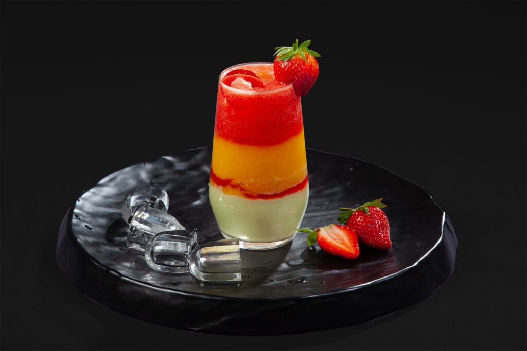 Vibrant layered strawberry and orange juice on ceramic plate with ice cubes and fresh strawberries.