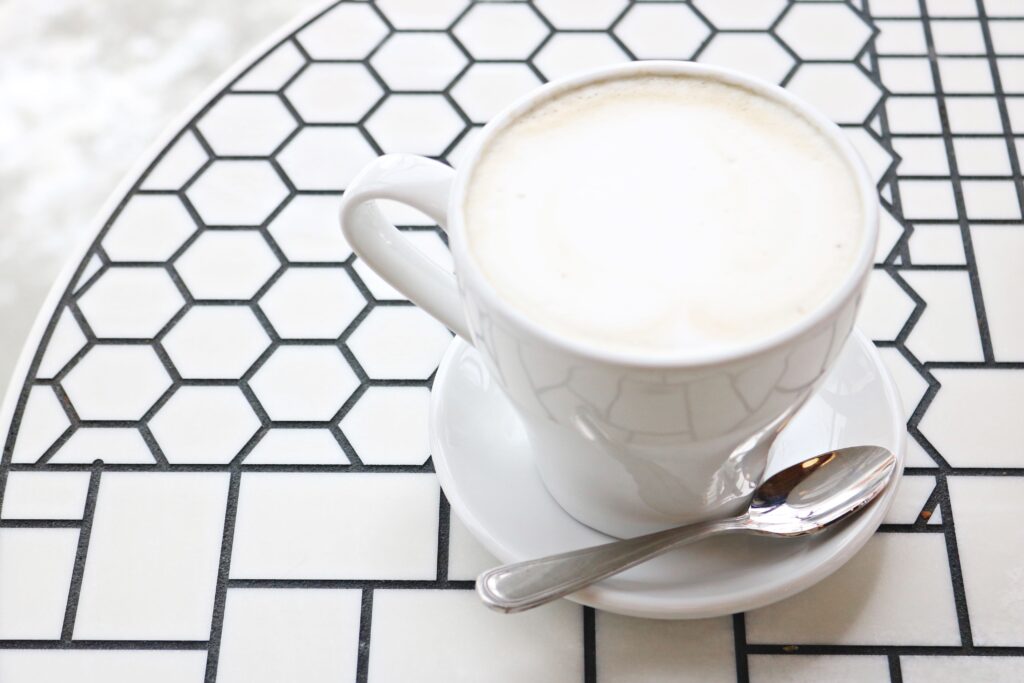 A coffee cup with cappuccino on a geometric ceramic table, accompanied by a spoon.