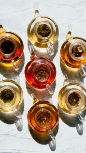 Top view of assorted herbal teas in glass teapots casting shadows on a marble surface.