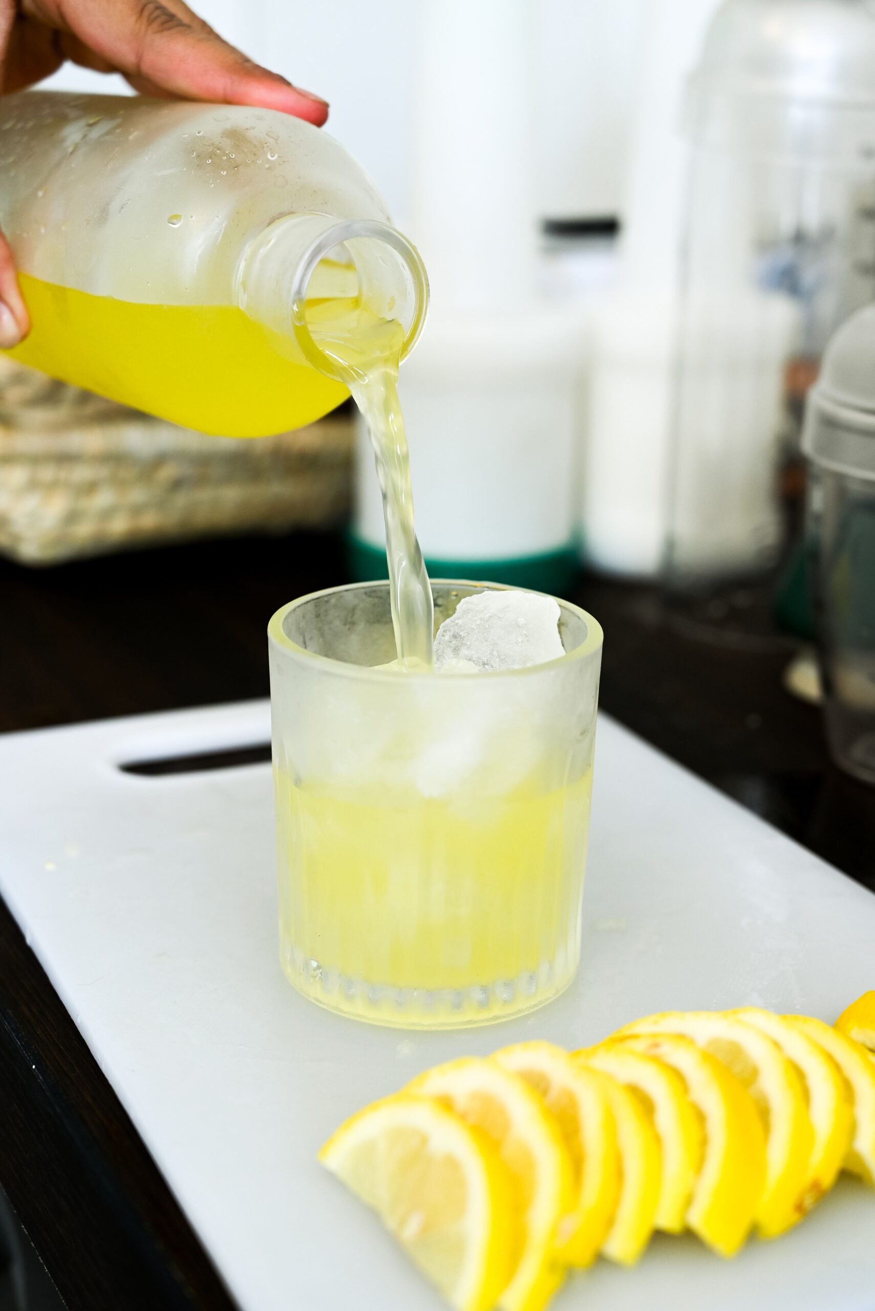 Hand pouring refreshing lemon juice into a glass on a kitchen countertop, perfect summer drink.