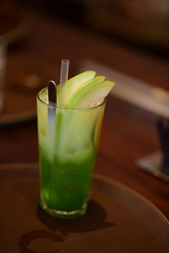 Tall glass of green apple mocktail garnished with apple slices, perfect for a summer refreshment.