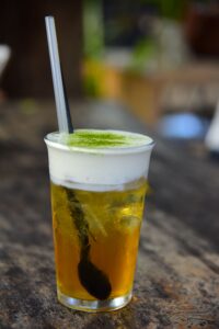 Refreshing iced green tea with a foamy top and straw on a rustic table, perfect for a summer drink.