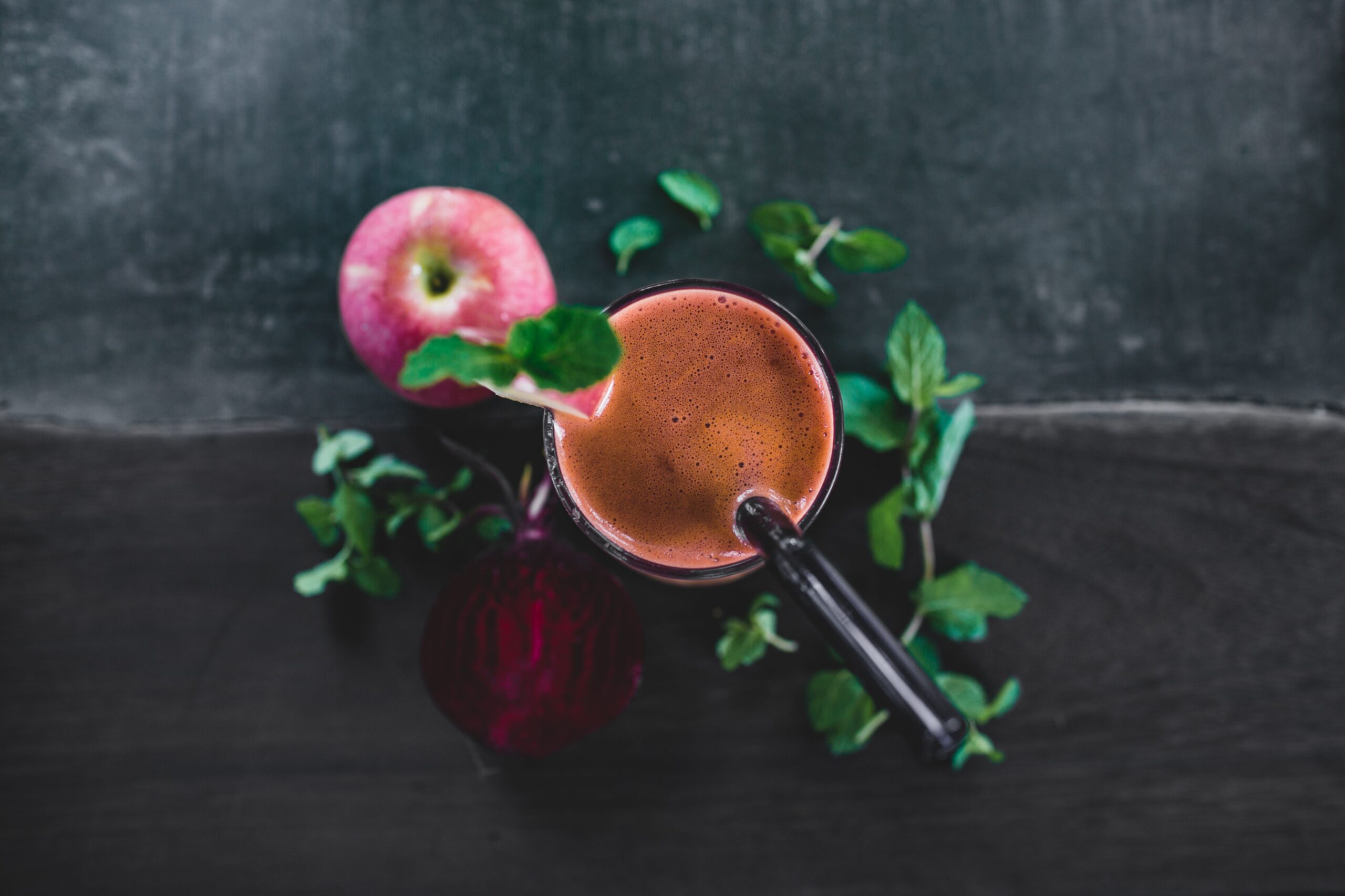 Top view glass of cold pressed juice composed with fresh apple and beetroot and decorated with mint leaves