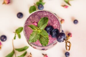 Refreshing beverage with blueberries, mint, and rose petals served on crushed ice, perfect for a warm day.