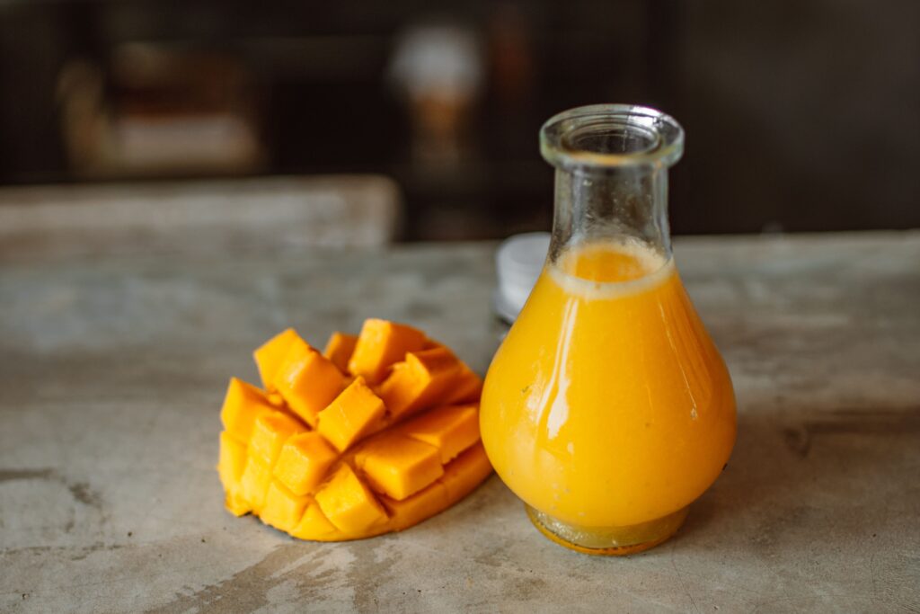 Sliced mango and fresh juice in glass carafe on rustic table.