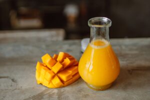 Sliced mango and fresh juice in glass carafe on rustic table.