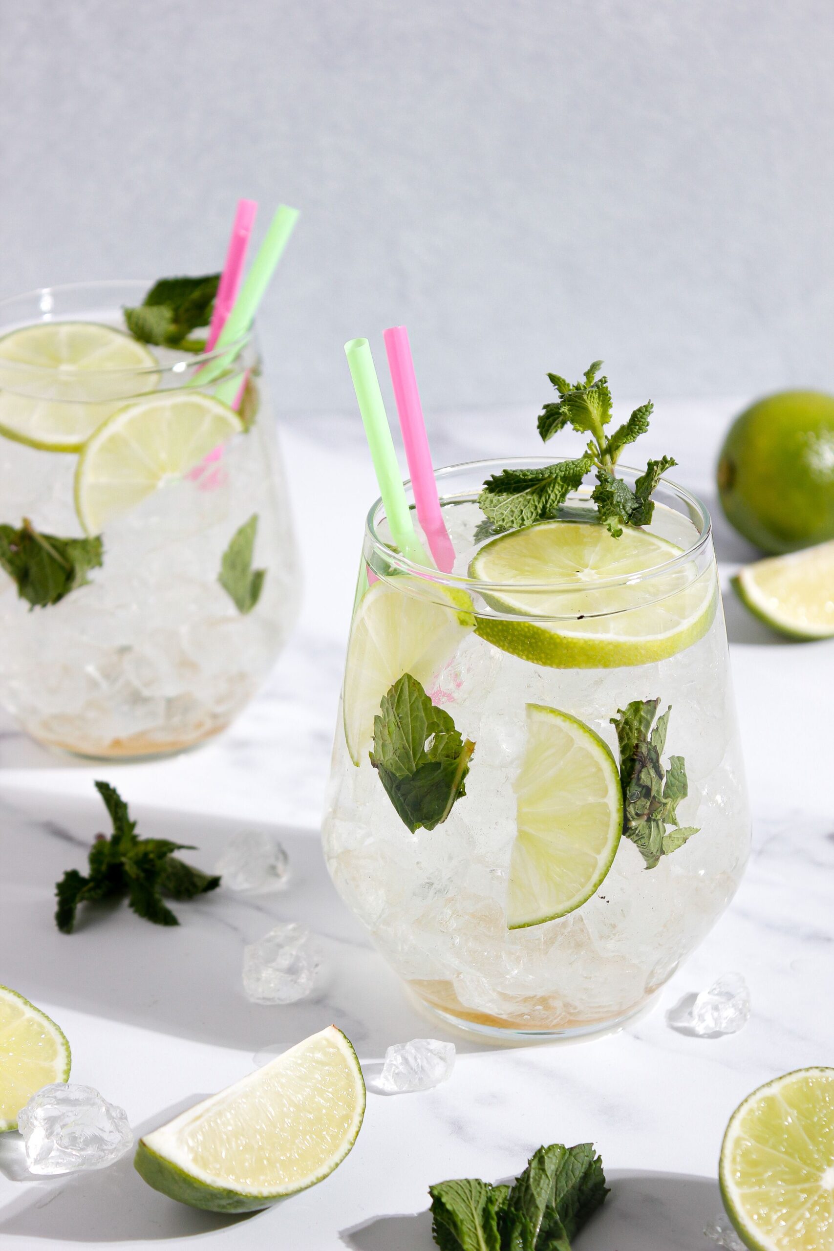 Close-up of mojito cocktails with lime slices, mint, and ice on a sunny day.