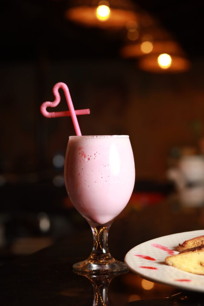 A tempting strawberry milkshake in a glass with a coiled straw on a restaurant counter.