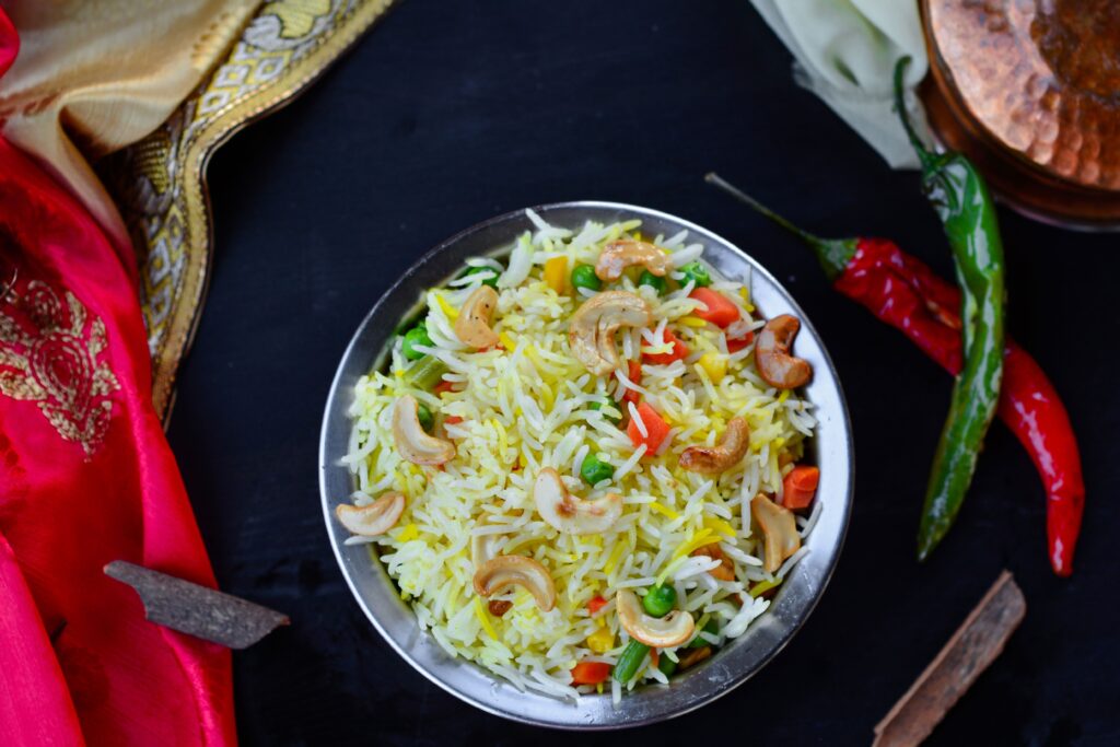 A vibrant, colorful Indian fried rice dish with cashews, chilies, and vegetables in a metal bowl.