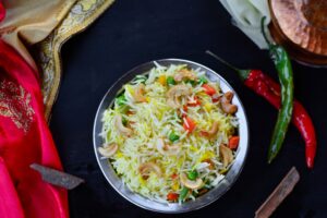 A vibrant, colorful Indian fried rice dish with cashews, chilies, and vegetables in a metal bowl.