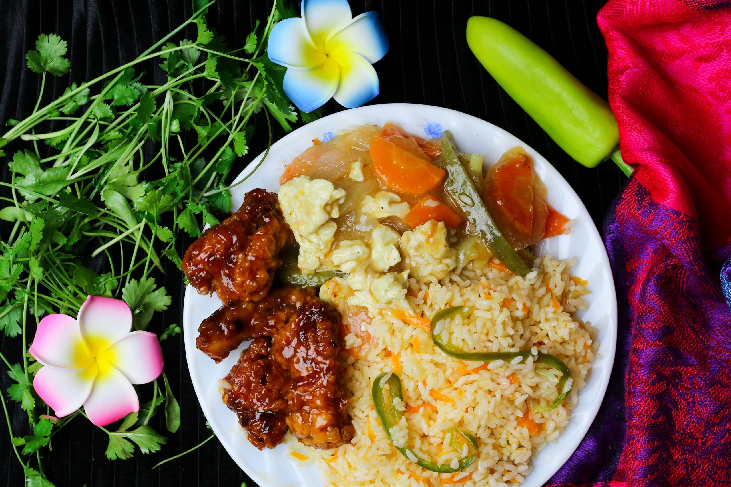 Vibrant plate of fried rice, chicken, and vegetables with decorative flower petals.
