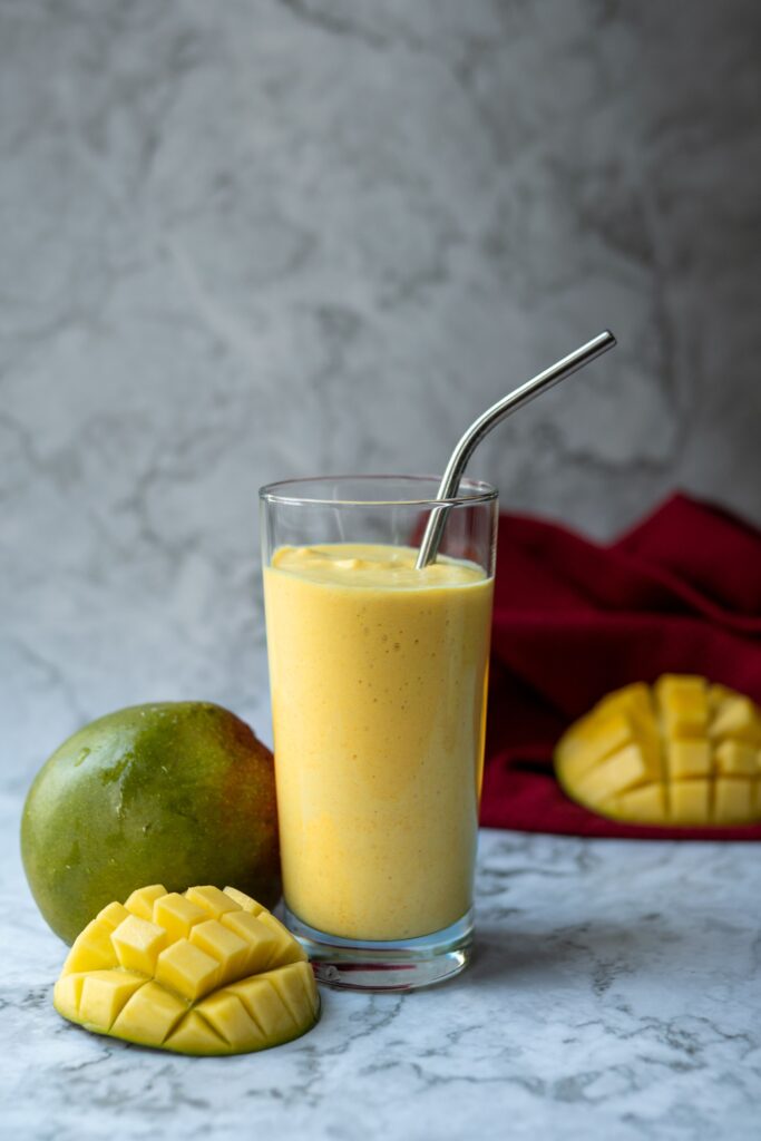 Delicious mango smoothie in a glass with metal straw and fresh mango slices.